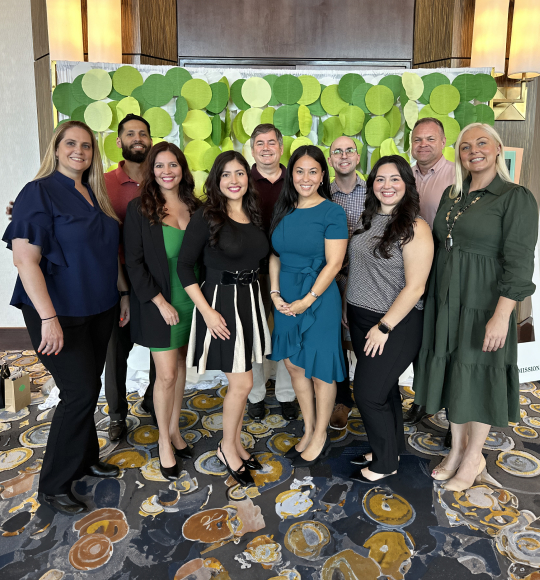 The TAM team standing in front of a banner made of green circles at a community event