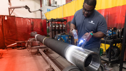 A TAM engineer using a light to help him spray coating across a pipe