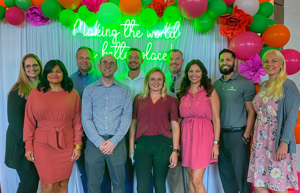 The TAM team standing in front of a neon sign at a community event