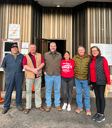 TAM team members in winter clothing standing together indoors for a group picture at a community event