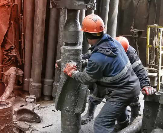 Two muddy oil workers twisting a drill into the ground