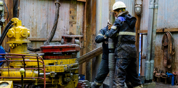 Two oil rig workers tightening a pipe, covered in mud