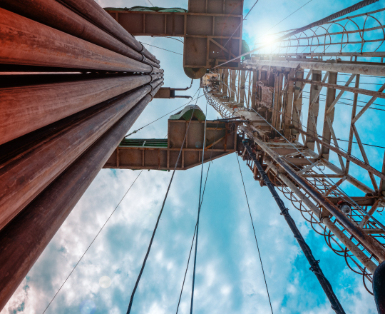 Looking up at the piping running alongside a drill tower of an oil derrick