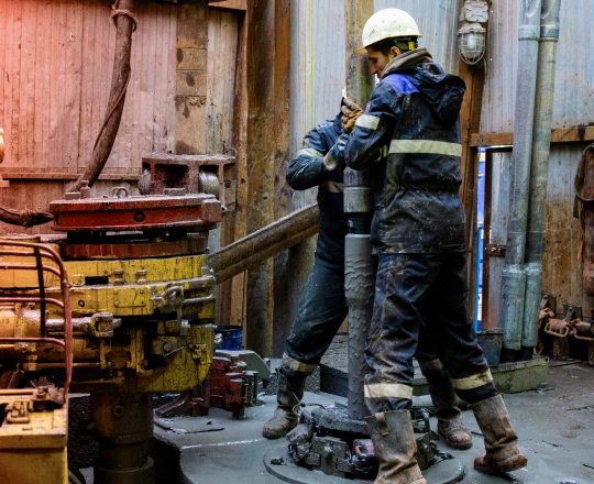 Two oil rig workers tightening a pipe, covered in mud