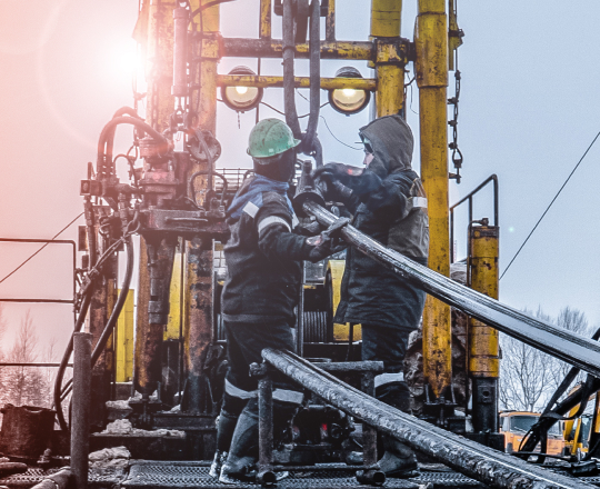 Two muddy rig workers plugging in tubing to a drill setup