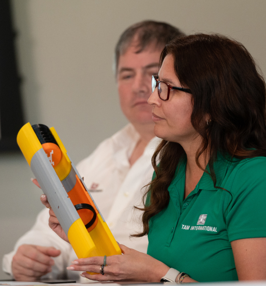 A TAM sales representative holding a yellow part to a downhole tool