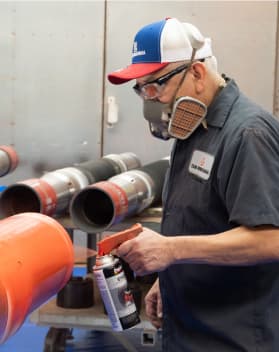 A TAM team member spray painting a pipe orange